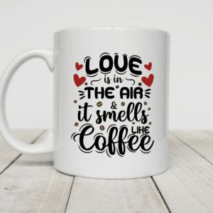 Witte koffiemok met tekst “Love is in the air & it smells like coffee” met rode hartjes en koffieboontjes